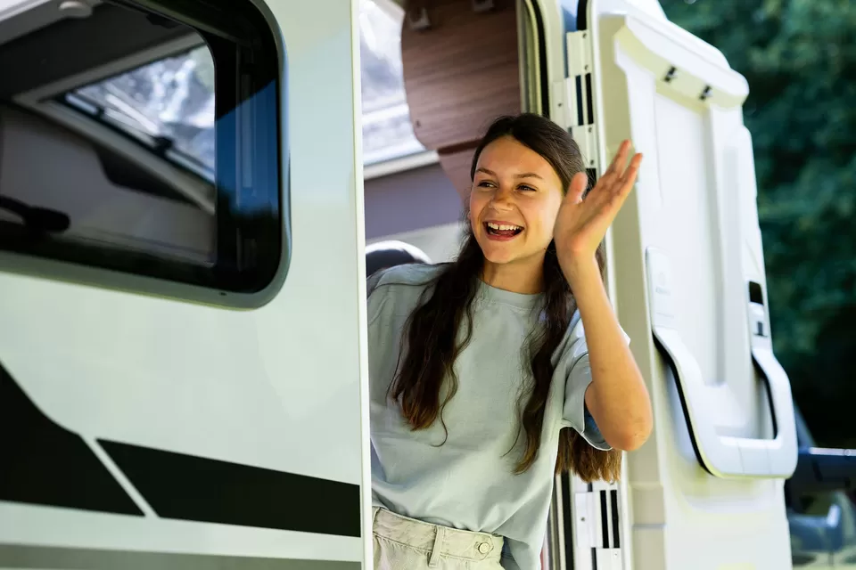 Vrouw zwaait vrolijk bij een camper, klaar voor haar volgende kampeervakantie