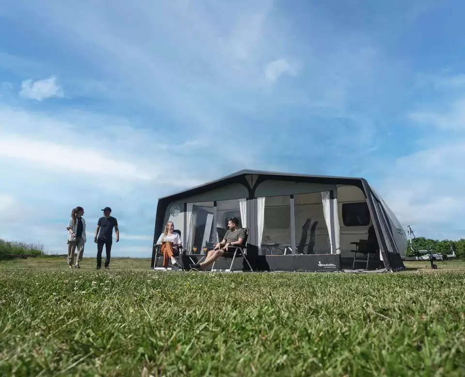 Groep mensen ontspant bij een grote voortent naast een caravan op een grasveld