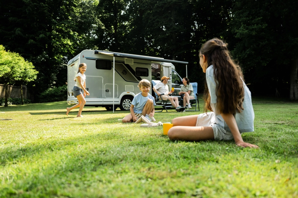 Gezin met kinderen ontspant voor hun camper op een groene camping