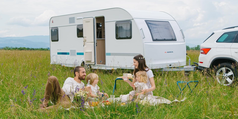 Gezin geniet van een picknick voor hun Adria caravan op een zomerse dag